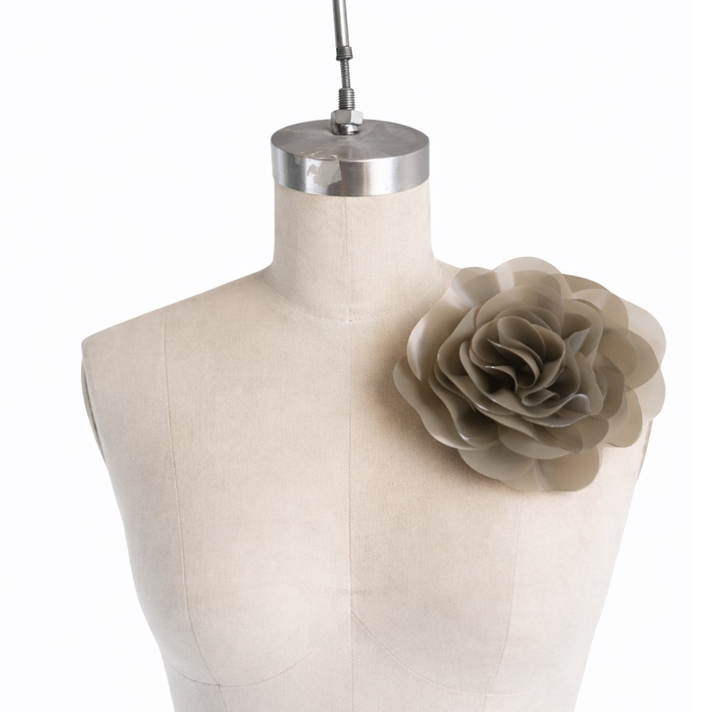 A Vex Latex dress form mannequin displays a large sculptural flower attached to its left shoulder with an oversized industrial safety pin, set against a plain white background.
