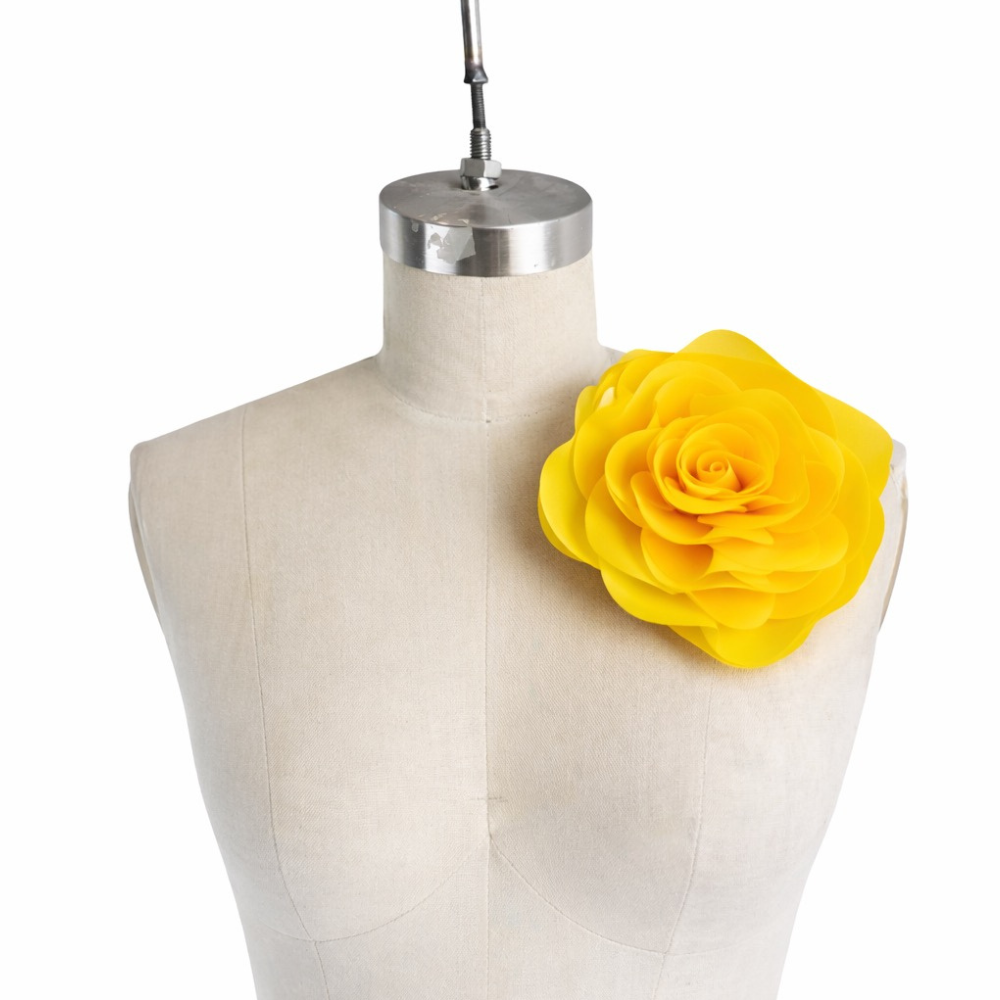 A Vex Latex dress form mannequin showcases a large, hand-crafted bright yellow floral pin on its left shoulder, set against a plain white background.