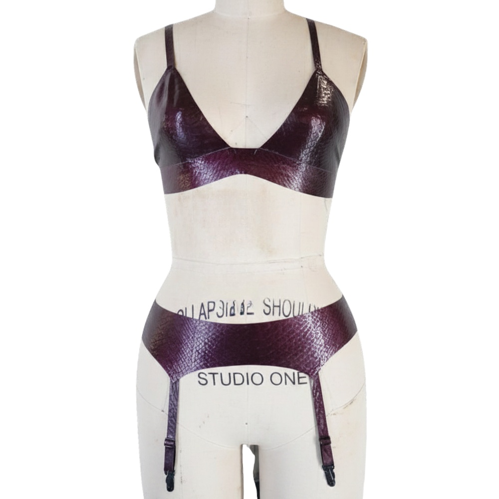 A dress form displays a shiny, dark purple faux snakeskin lingerie set by Vex Latex, featuring a bralette and garter belt. The mannequin is labeled STUDIO ONE, with a "Ready to Ship" banner on the plain white background.