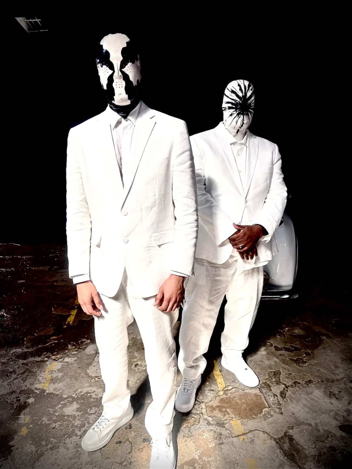 Two individuals in white suits with mask-like face coverings standing on a dark street.